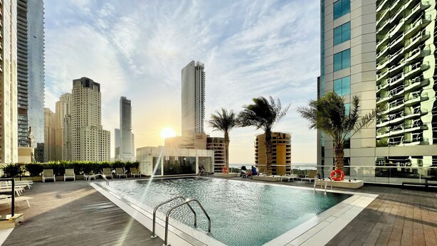 A rooftop pool area with a view of high-rise buildings and a sunset. - Settler.Homes, Breathtaking 2BR Marina, HighFloor (Dubai)