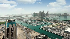A marina with numerous boats, a large building with a distinctive green roof, and a city skyline in the background. - Settler.Homes, Breathtaking 2BR Marina, HighFloor (Dubai)