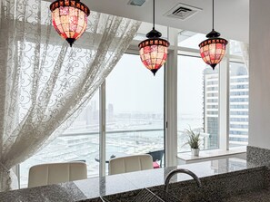 A modern hotel room with a large window, decorative curtains, and two hanging lamps. - Settler.Homes, Breathtaking 2BR Marina, HighFloor (Dubai)