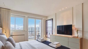 Ein modernes Hotelzimmer mit einem großen Bett, einem Flachbildfernseher, Blick auf die Stadt und einem minimalistischen Design.