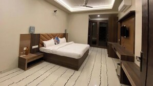 A modern hotel room with a bed, bedside table, TV, and a ceiling fan. - Hotel Amba Ambience (Hathras)