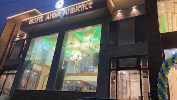 A hotel with a modern facade, large glass windows, and a visible chandelier inside. - Hotel Amba Ambience (Hathras)