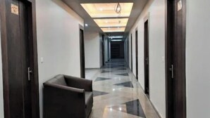 A hotel hallway with a sofa, dark wooden doors, and a patterned floor. - Hotel Amba Ambience (Hathras)