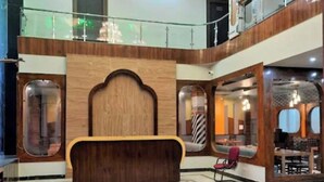 A lobby with a central wooden reception desk, a tiled floor, and a glass railing overlooking the lower level. - Hotel Amba Ambience (Hathras)