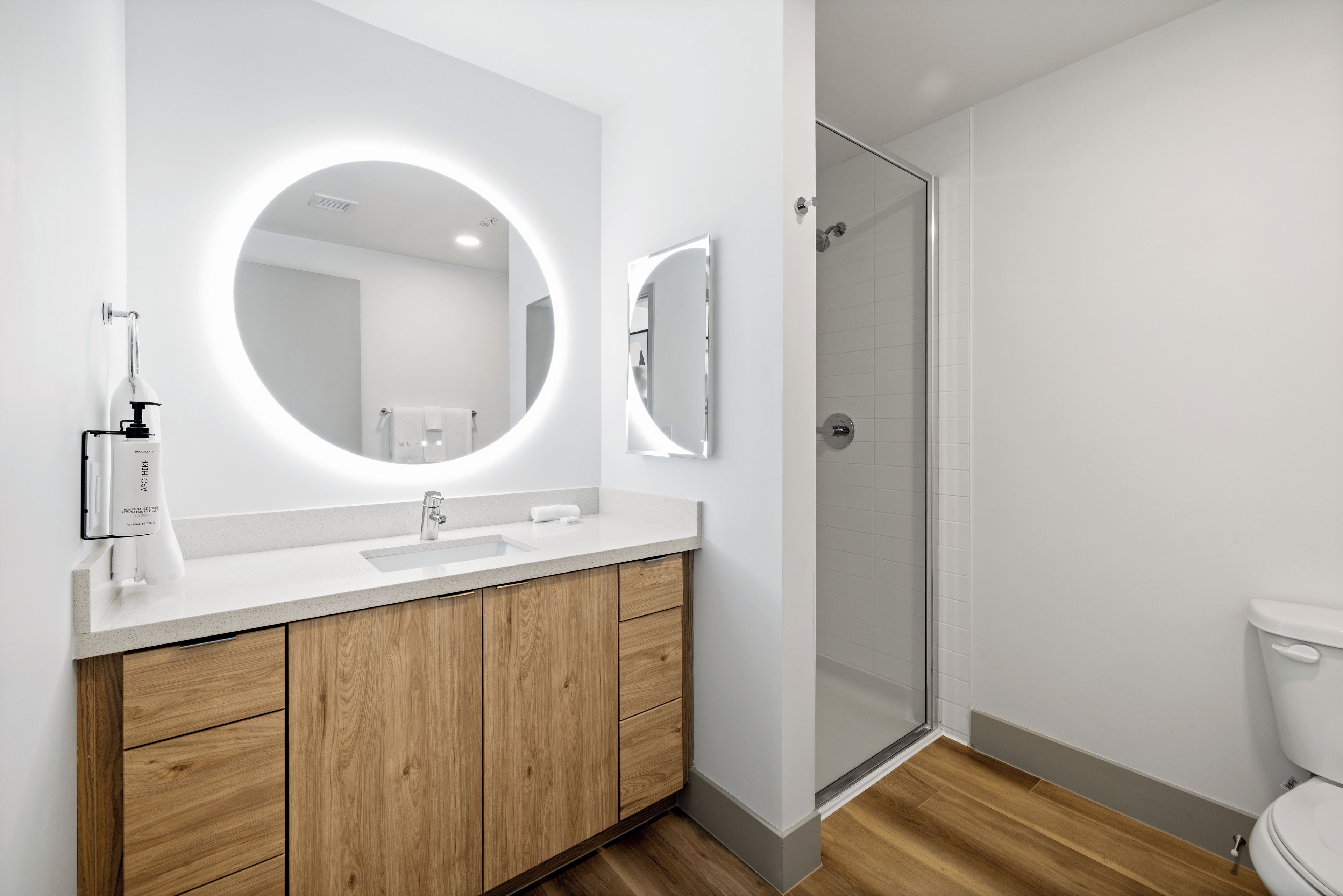 A modern bathroom with a white vanity, a round mirror, and a glass shower enclosure.