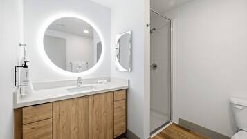 A modern bathroom with a white vanity, a round mirror, and a glass shower enclosure.