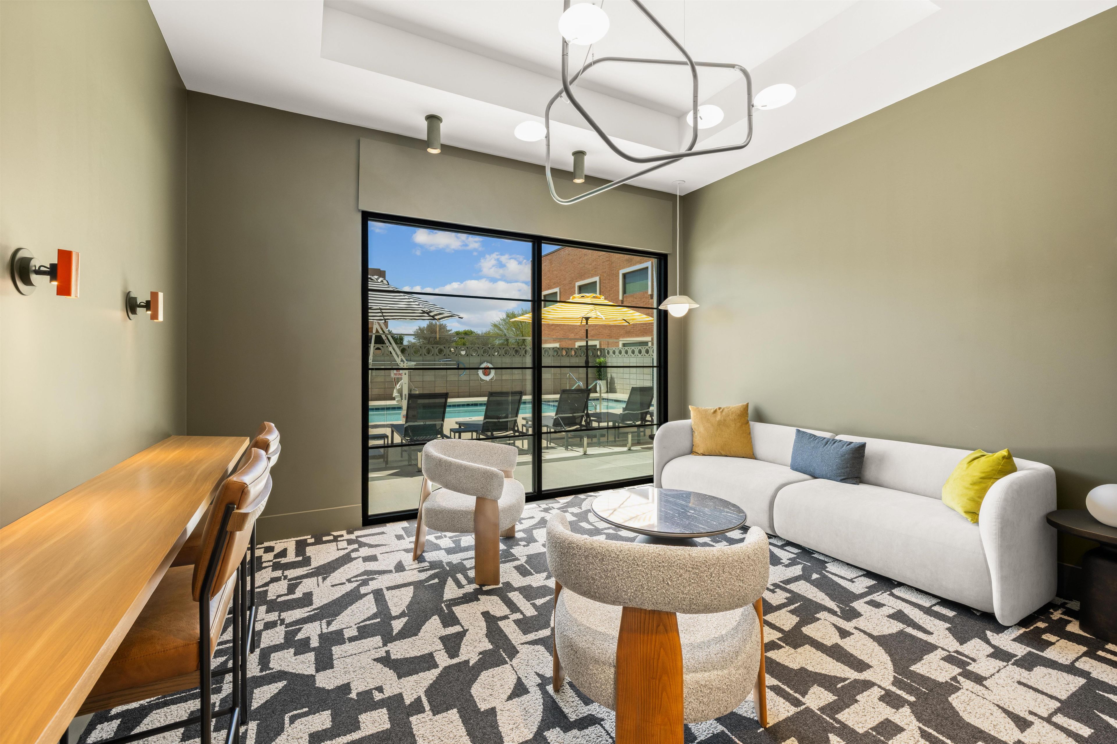 Un área de estar moderna con vista a la piscina, una mesa de madera, un sofá y una alfombra estampada.