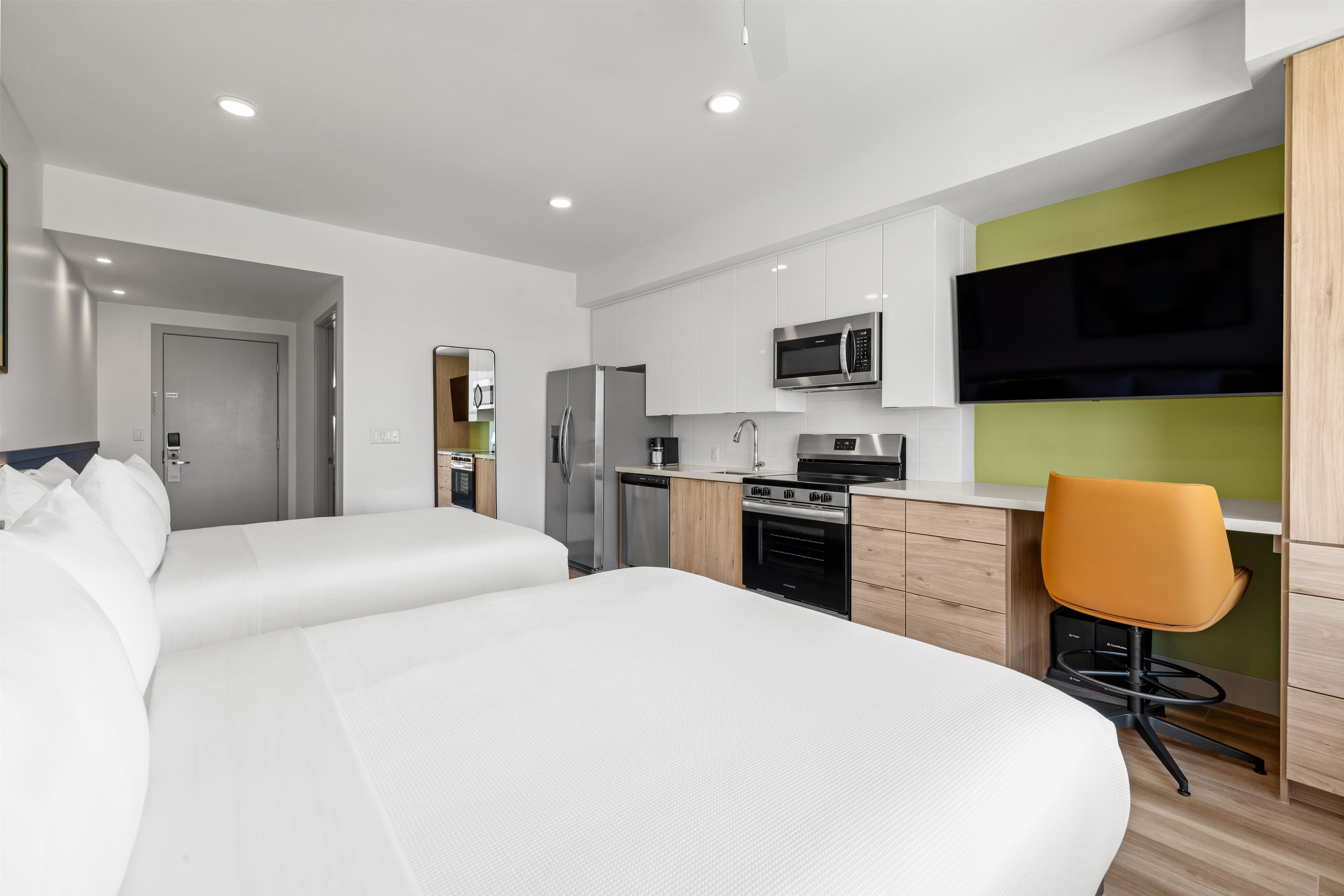 Ein modernes Hotelzimmer mit Bett, Schreibtisch, Stuhl, Mikrowelle, Kühlschrank und Fernseher.