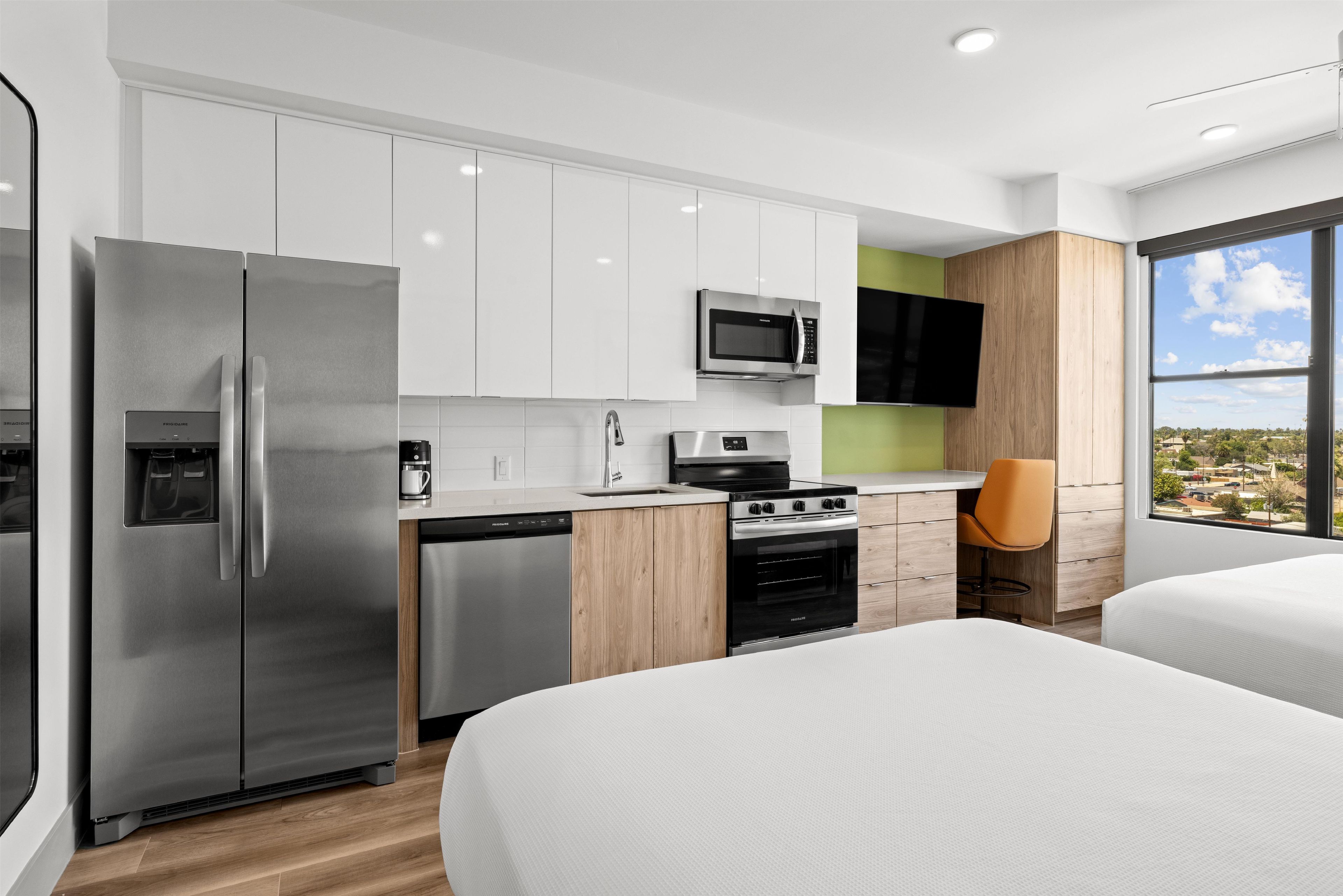A modern kitchen with a refrigerator, microwave, stove, and dishwasher. There is a window with a view of the outside.