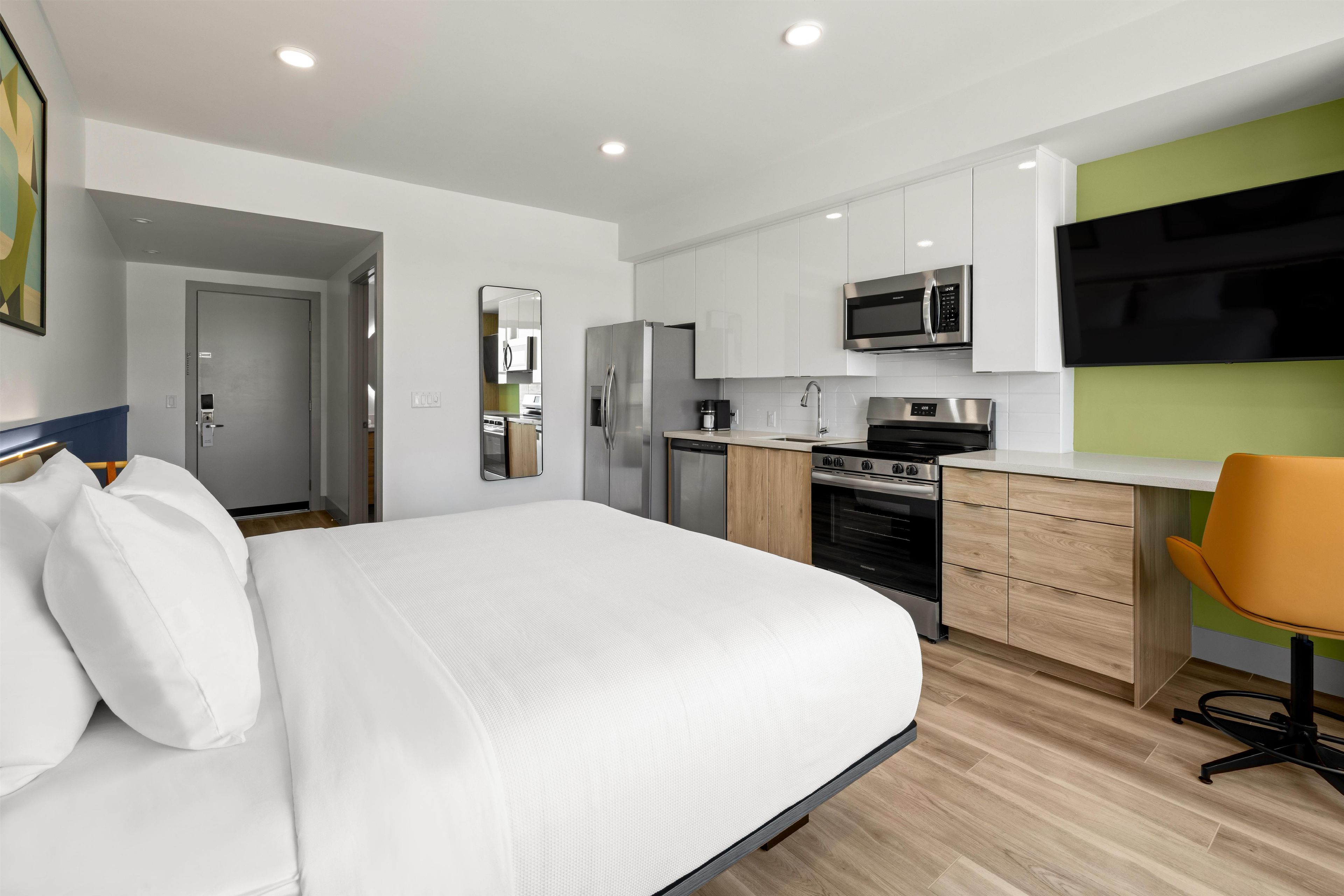 A modern hotel room with a bed, a desk, a microwave, a coffee maker, and a TV.