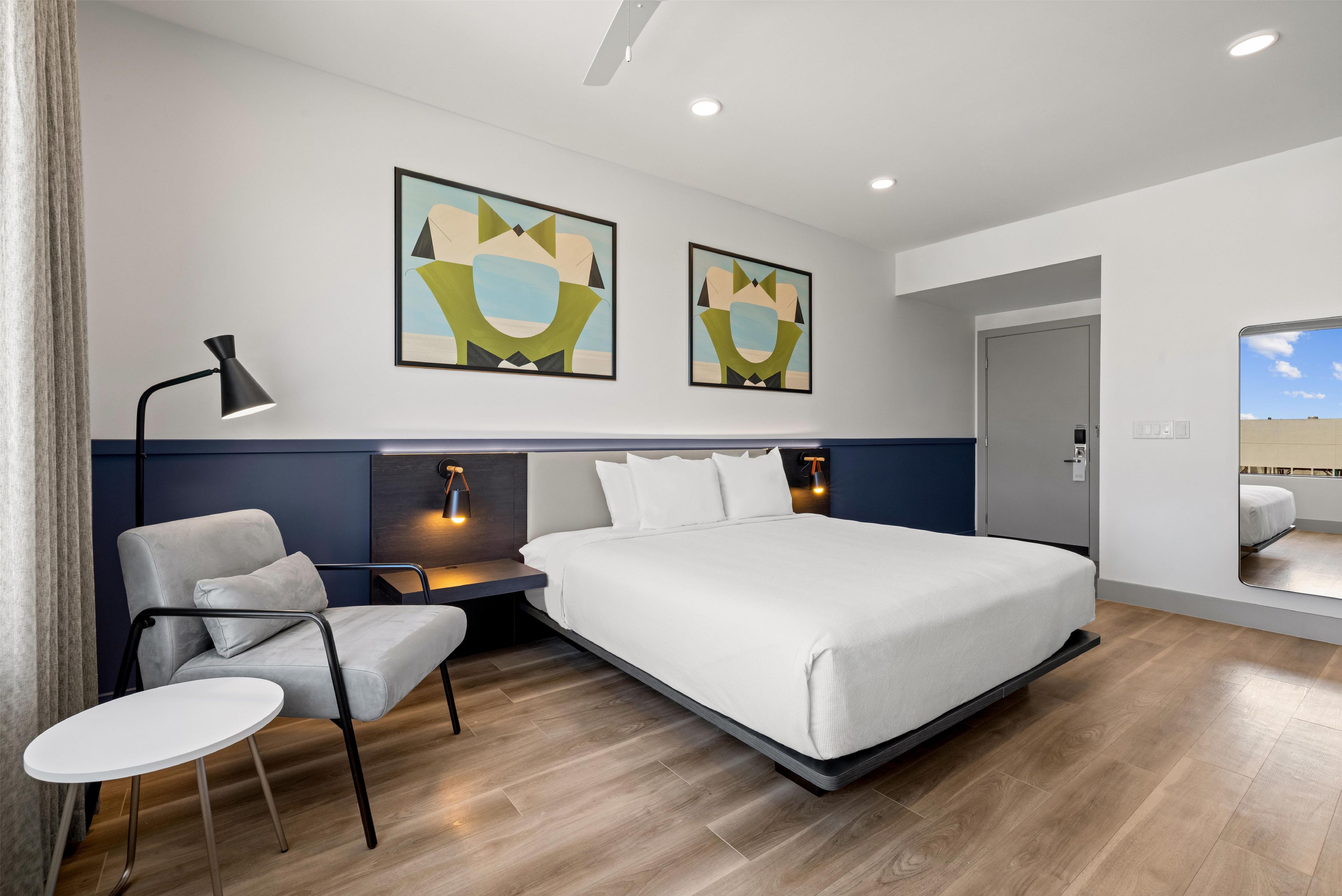 Habitación de hotel moderna con una cama grande, un escritorio, una silla y dos obras de arte en la pared.