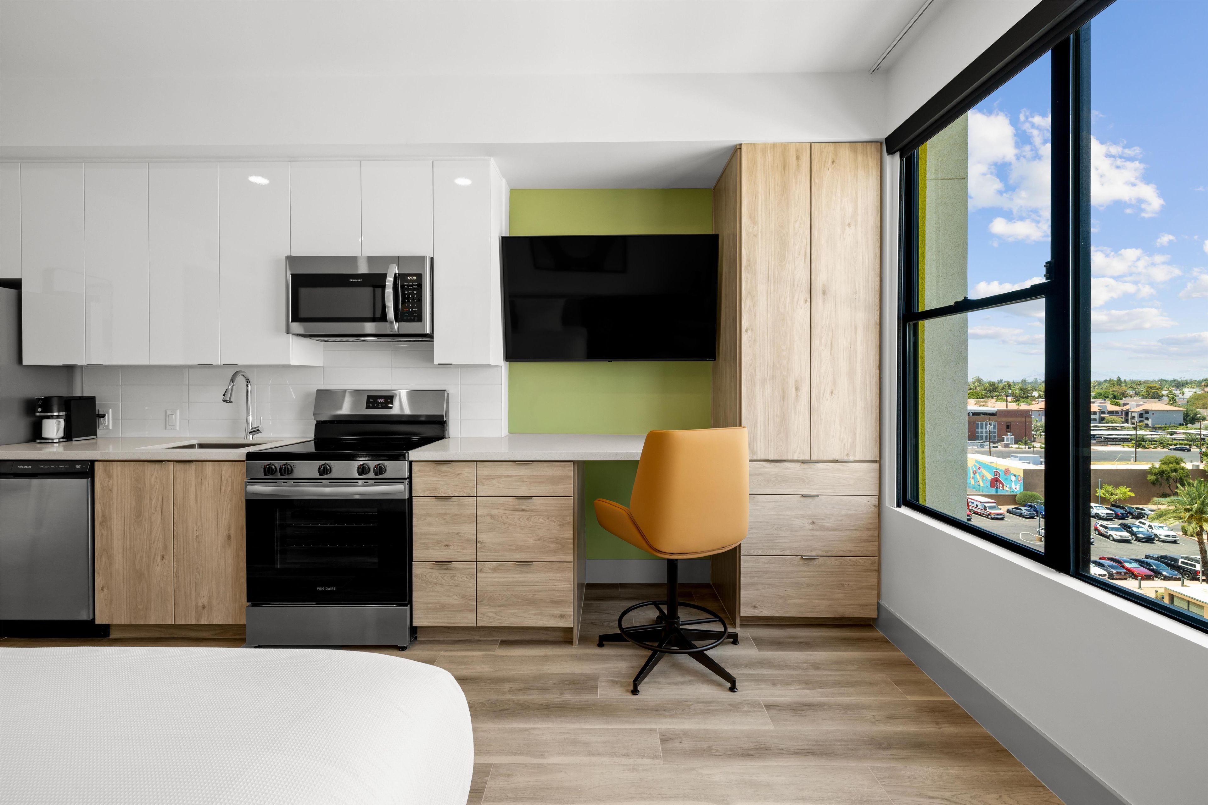 A modern kitchen with white cabinets, a microwave, stove, and a large window with a view of a parking lot.