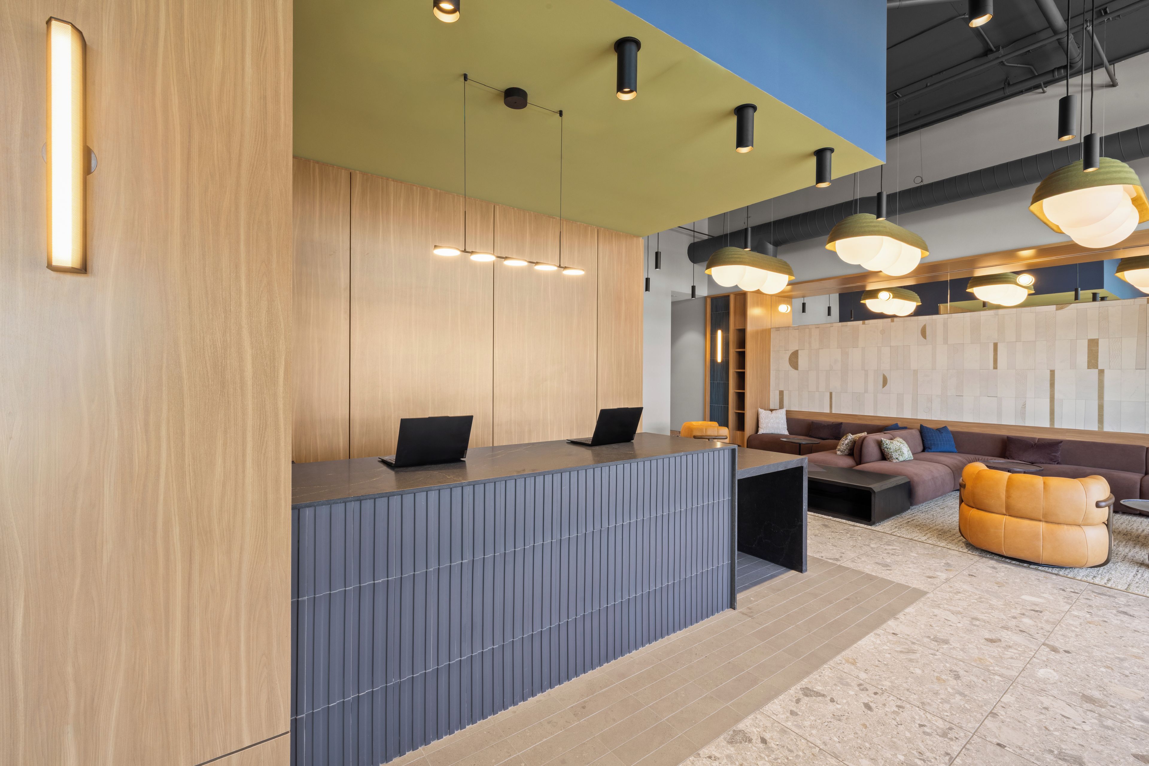 A modern reception desk with a laptop, a seating area with a sofa and ottoman, and pendant lighting.