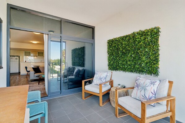 A modern living area with a sliding glass door leading to a balcony, a green wall, and a dining table with chairs.