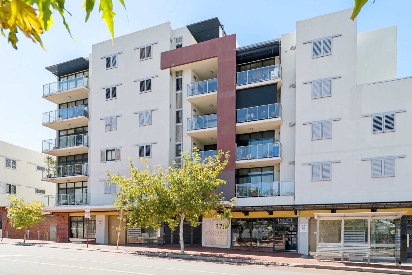 A multi-story apartment building with balconies, a bus stop, and a storefront.