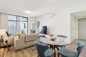 A modern living room with a glass dining table, a sofa, and a TV. - The Beaufort Street Nook (Perth)