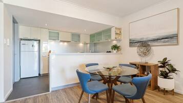 A modern kitchen with white cabinets, a central island, and blue chairs around a glass table.