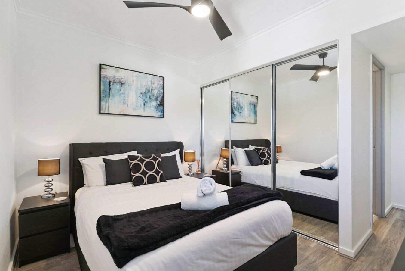 A modern bedroom with a large bed, two bedside tables, a ceiling fan, and a large mirror.