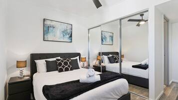 A modern bedroom with a large bed, two bedside tables, a ceiling fan, and a large mirror.