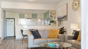 A modern living room with a sofa, two armchairs, a glass coffee table, and a kitchen in the background. - The Beaufort Street Nook (Perth)