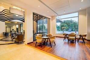 A modern hotel lobby with a large mirror, a seating area with chairs and sofas, and a view of the outdoors through large windows. - Sunday Resort & Spa Manesar Gurugram (Gurgaon)