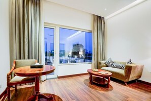 A hotel room with a large window, a sofa, a wooden chair, and a small table. - Sunday Resort & Spa Manesar Gurugram (Gurgaon)