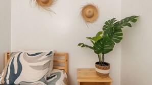 A room with a bed, a wooden nightstand, a potted plant, and two wall-mounted hats. - Walkable Rincón Paradise near Plaza & Beaches w/ Carport (Rincon)