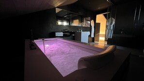 Une salle de spa moderne dotée d’une grande baignoire, d’un banc en bois et d’une paroi en verre.