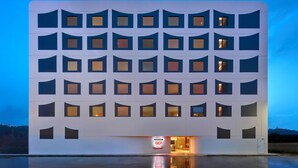 Een modern hotel met een raster van ramen en een reflecterend zwembad ervoor.