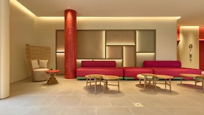 Een moderne zithoek met een rode bank, rieten stoelen en kleine ronde tafels.