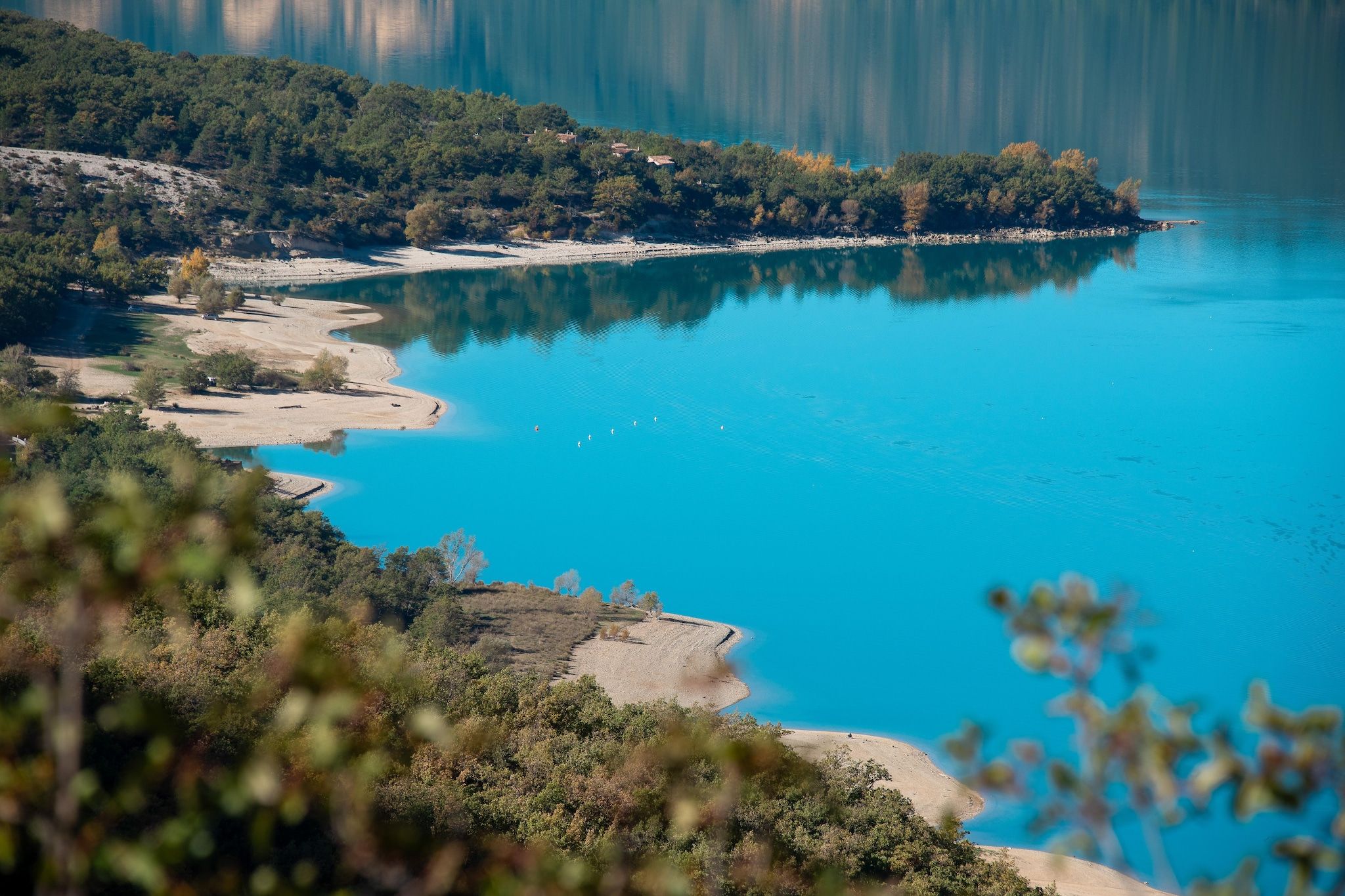 Een kustlandschap met een helderblauw meer, zandstranden en weelderige begroeiing.