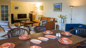A living room with a wooden dining table set for a meal, a sofa, a television, and a floor lamp. - Gîte Guillaume with swimming pool (Carcès)