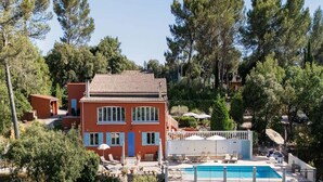 A two-story building with a tiled roof, surrounded by trees and a swimming pool with lounge chairs. - Gîte Guillaume with swimming pool (Carcès)