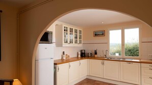 A kitchen with white cabinets, a wooden countertop, a built-in microwave, a coffee maker, and a window with a view of greenery. - Gîte Guillaume with swimming pool (Carcès)