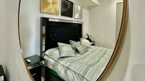 A bedroom with a bed, bedside tables, a nightstand, and wall art.