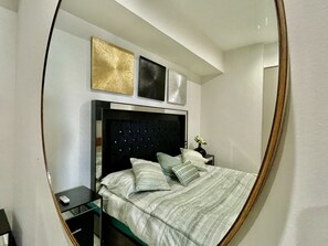 A bedroom with a bed, bedside tables, a nightstand, and wall art. - Sunset Malecon View (Mazatlán)