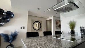 A modern kitchen with granite countertops, a stainless steel range hood, and a dining area with black chairs.