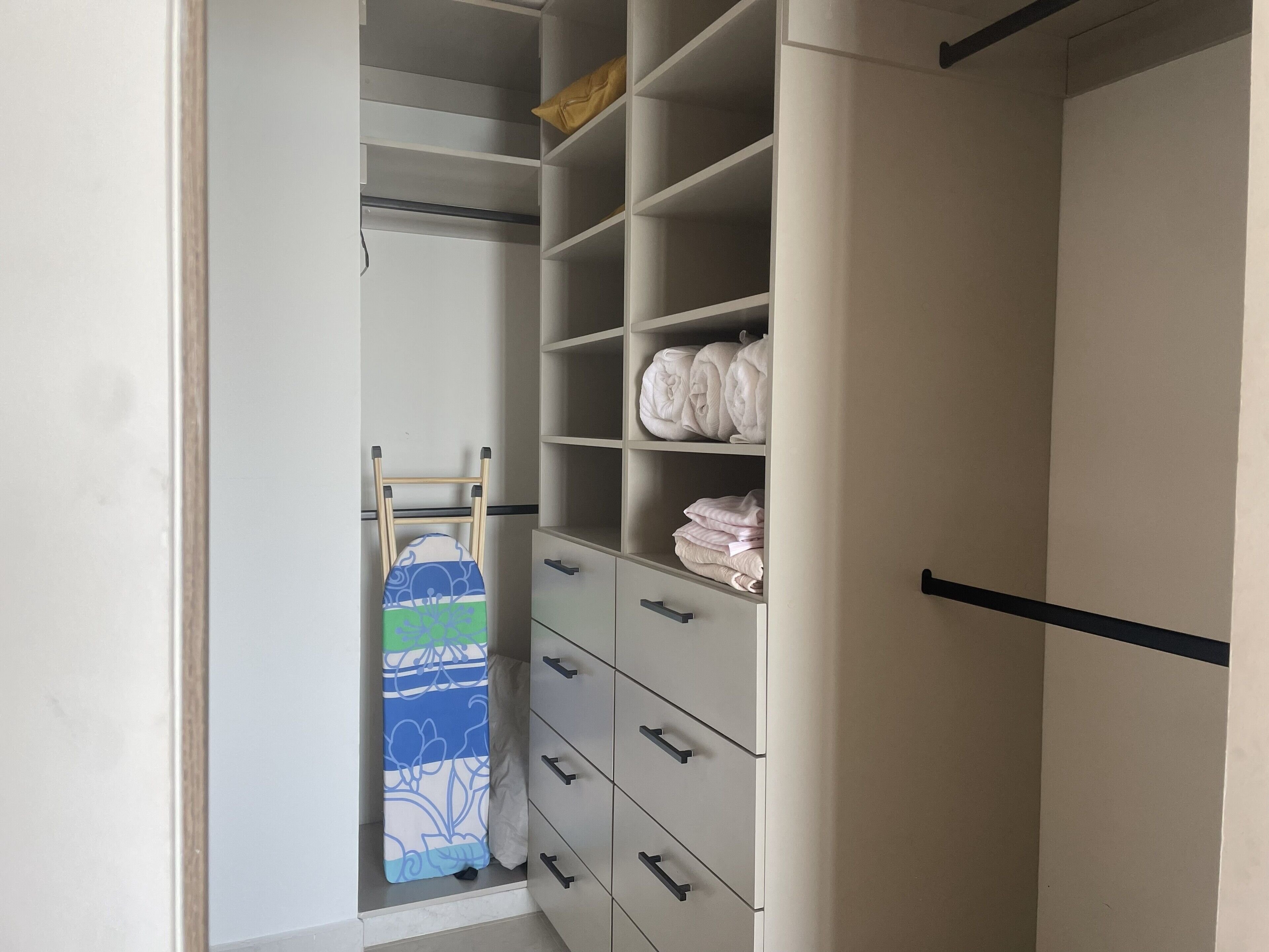Um closet espaçoso com várias prateleiras e gavetas, contendo toalhas dobradas e um chuveiro com cortina colorida.