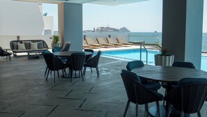 A modern outdoor lounge area with a pool, seating, and a view of the sea.