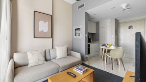 A modern living room with a sofa, a coffee table, and a TV. There is a kitchen area with a dining table and chairs. - Canal View 1BR Near Business Bay Metro (Dubai)