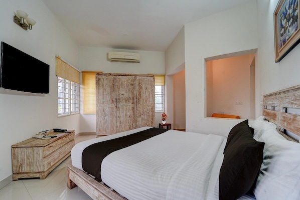 Une chambre à coucher avec un lit, une commode en bois, un téléviseur et une fenêtre avec des stores.