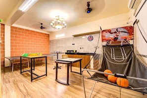 Ein Zimmer mit Backsteinwand, Basketballkorb, Tischtennisplatte und einem weiteren Tischtennistisch.