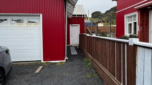 Un edificio rojo con puerta de garaje blanca, cerca de madera y camino de grava.