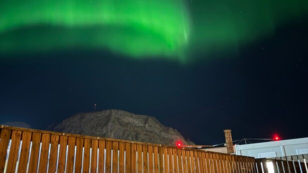 Una terraza de madera con asientos, una montaña al fondo y las auroras boreales en el cielo.