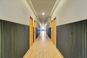 A long, narrow hallway with wooden flooring, flanked by vertical acoustic panels and doors on both sides.