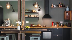 Une cuisine moderne dotée d’un îlot central, de tabourets en bois et de divers ustensiles de cuisine rangés sur des étagères.
