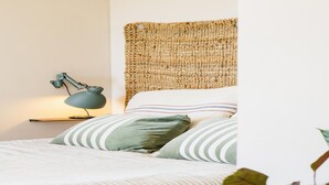 Un lit bien fait, avec une literie à rayures, une tête de lit en osier et une lampe de chevet.