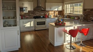 A modern kitchen with white cabinetry, a central island, and a window providing natural light. - Mountain Blue Guest house (Golden Valley)