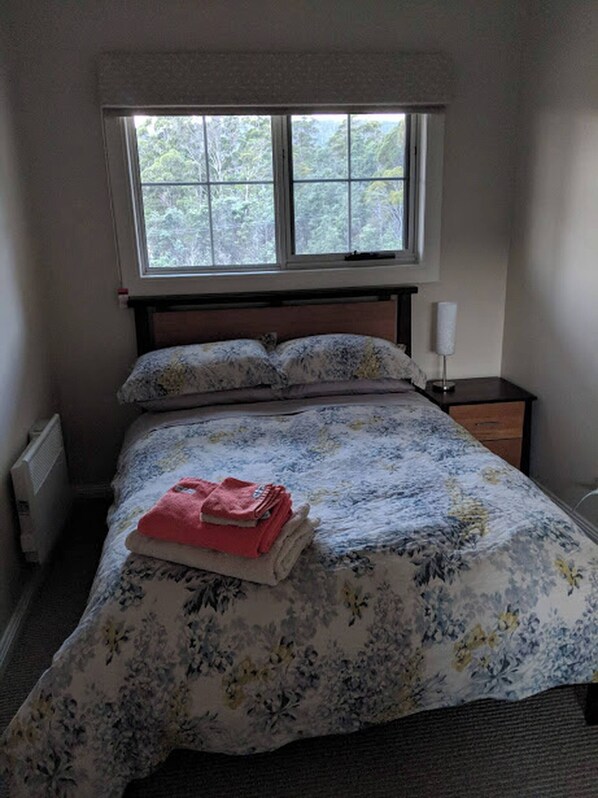 Un dormitorio con cama, ventana, mesita de noche y radiador.