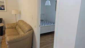A room with a beige sofa, a lamp, a bed with a patterned bedspread, and a hanging light fixture. - A charming countryside accommodation near Malmö (Oxie)